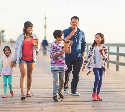 A family walks on a pier eating ice cream.